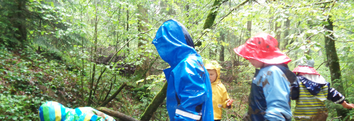 Kinder in Regenjacken spielen im Wald.